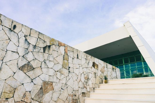 A contemporary building facade featuring a stone wall and angular architecture under a clear sky.